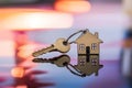 House shaped keys on reflective surface with blurred vibrant colors, symbolizing homeownership at dusk