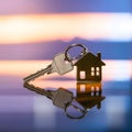 House shaped keys on reflective surface with blurred vibrant colors, symbolizing homeownership at dusk