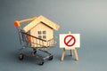 House in the shopping cart and the sign of the ban NO. Inaccessible and expensive housing. Seizure and freezing of assets