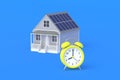 House with solar panels on roof near alarm clock on blue background