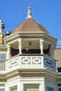 House spire or turret with metal tip and white balcony with accent paint and wooden pannels in midday sun with blue sky