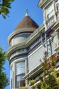 House spire or turret with visible decorative facade and brown roof with tiles and front yard trees in suburbs with blue