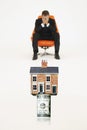 House on top of roll of bills with worried businessman on chair representing expensive real estate Royalty Free Stock Photo