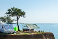 A house on wheels and a canopy under a tree on a cliff by the sea