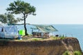 A house on wheels and a canopy under a tree on a cliff by the sea