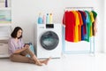 House wife sitting with cloth washing machine on floor watching smartphone during doing chore