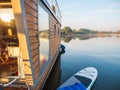 Houseboat on a river in a early morning moored on a pier with paddleboard. floating house is a pleasant place for rent for