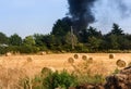 Housefire in the distance after a field of rolled Hay Royalty Free Stock Photo