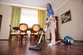 Delightful happy Arabic Muslim young woman or housewife with vacuum cleaner, vacuuming the floor at home. Household, housework and Royalty Free Stock Photo