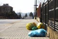 Household rubbish in multicolored sorting bags lies on a city street near the fence of private territory, awaiting export from the