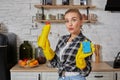 Professional young woman wearing rubber protective yellow gloves holding bottle cleaners in the kitchen. Royalty Free Stock Photo