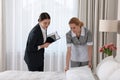 Housekeeping manager with tablet checking maid`s work in hotel bedroom