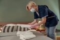 Housemaid in mask putting stack of fresh white bath towels on bed sheet. Room service concept Royalty Free Stock Photo