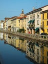 Houses along the Naviglio Grande in Milan on a bright summer morning, reflected in the calm water of the canal