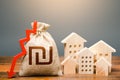 Houses and israeli shekel money bag with down arrow. Reducing maintaining cost, energy efficiency, saving. Realty crisis. Low Royalty Free Stock Photo