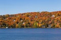 Houses nestled in colourful fall foliage on the side of a mountain overlooking a lake