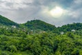 Houses among trees on hill in Black Sea region during a cloudy day and the sun can be seen behind clouds Royalty Free Stock Photo