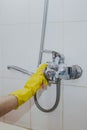 Housewife cleaning bathroom tap and shower Tap. Maid in yellow protective gloves washing dirty bath tap. Hands of woman washing Royalty Free Stock Photo