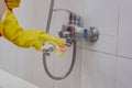 Housewife cleaning bathroom tap and shower Tap. Maid in yellow protective gloves washing dirty bath tap. Hands of woman washing Royalty Free Stock Photo