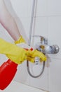 Housewife cleaning bathroom tap and shower Tap. Maid in yellow protective gloves washing dirty bath tap. Hands of woman washing Royalty Free Stock Photo