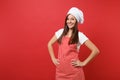 Housewife female chef cook or baker in striped apron, white t-shirt, toque chefs hat isolated on red wall background Royalty Free Stock Photo