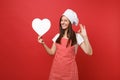 Housewife female chef cook or baker in striped apron, white t-shirt, toque chefs hat isolated on red wall background Royalty Free Stock Photo