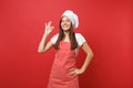 Housewife female chef cook or baker in striped apron white t-shirt, toque chefs hat isolated on red wall background Royalty Free Stock Photo