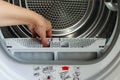 A housewife holds a lint trap from a front-loading tumble dryer. Woman`s hand