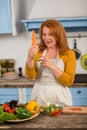 Housewife in the kitchen holding huge carrot. Royalty Free Stock Photo
