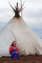 Housewife of nenets nomad tribe in national costume repairs a clothes in front of the family chum during autumn reindeer migration