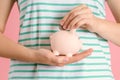 Housewife puts a coin in a pink piggy bank, close-up