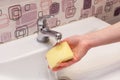 Housewife rinsing off a sponge for cleaning the bathroom under the running water from the hand basin Royalty Free Stock Photo