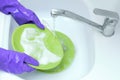 Housewife.Wash green plates under running water. Hands in protective rubber gloves Royalty Free Stock Photo