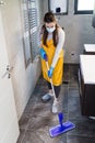Housewife wearing surgical mask and gloves doing chores at home by holding mopping stick. Coronavirus prevention concept Royalty Free Stock Photo