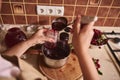 Housewife, woman confectioner pouring delicious freshly brewed cherry berry jam into sterilized glass jar at home kitchen Royalty Free Stock Photo