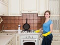 Housework and housekeeping concept - happy young woman with bottle of spray cleanser cleaning oven at home kitchen. Royalty Free Stock Photo