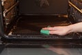 Housework and housekeeping concept. Scrubbing the stove and oven. Close up of female hand with green sponge cleaning the kitchen o