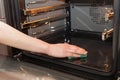 Housework and housekeeping concept. Scrubbing the stove and oven. Female hand with green sponge cleaning the kitchen oven..