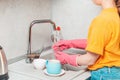 Housework. A woman in casual clothes and pink rubber gloves is washing tableware