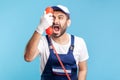 Housing maintenance call centre. Crazy handyman in overalls, safety gloves, shouting into retro phone handset Royalty Free Stock Photo