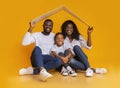 Black Family Sitting Under Symbolic Roof Dreaming Of New Home.