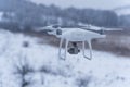 Hovering drone taking pictures of wild nature. Cold winter weather. Cloudy day with falling snow Royalty Free Stock Photo