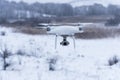 Hovering drone taking pictures of wild nature. Cold winter weather. Cloudy day with falling snow Royalty Free Stock Photo