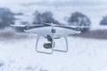 Hovering drone taking pictures of wild nature. Cold winter weather. Cloudy day with falling snow Royalty Free Stock Photo