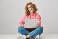 How comfortable to work wherever I want. Studio shot of sensual cute curly-haired woman working in laptop while sitting