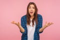 How could you? Portrait of indignant girl in checkered shirt raising hands asking what why, looking dissatisfied