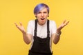 How could you? Portrait of outraged hipster woman standing in bewilderment with raised hands. yellow background, studio shot