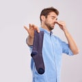 How old is this sock. Studio shot of a handsome young man holding an unpleasant smelling sock against a gray background.