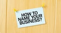 HOW TO NAME YOUR BUISINESS sign written on sticky note pinned on wooden wall