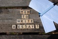 How to write a essay? Black capital letter words on wooden toy blocks on a natural garden table background with paper and pencil.